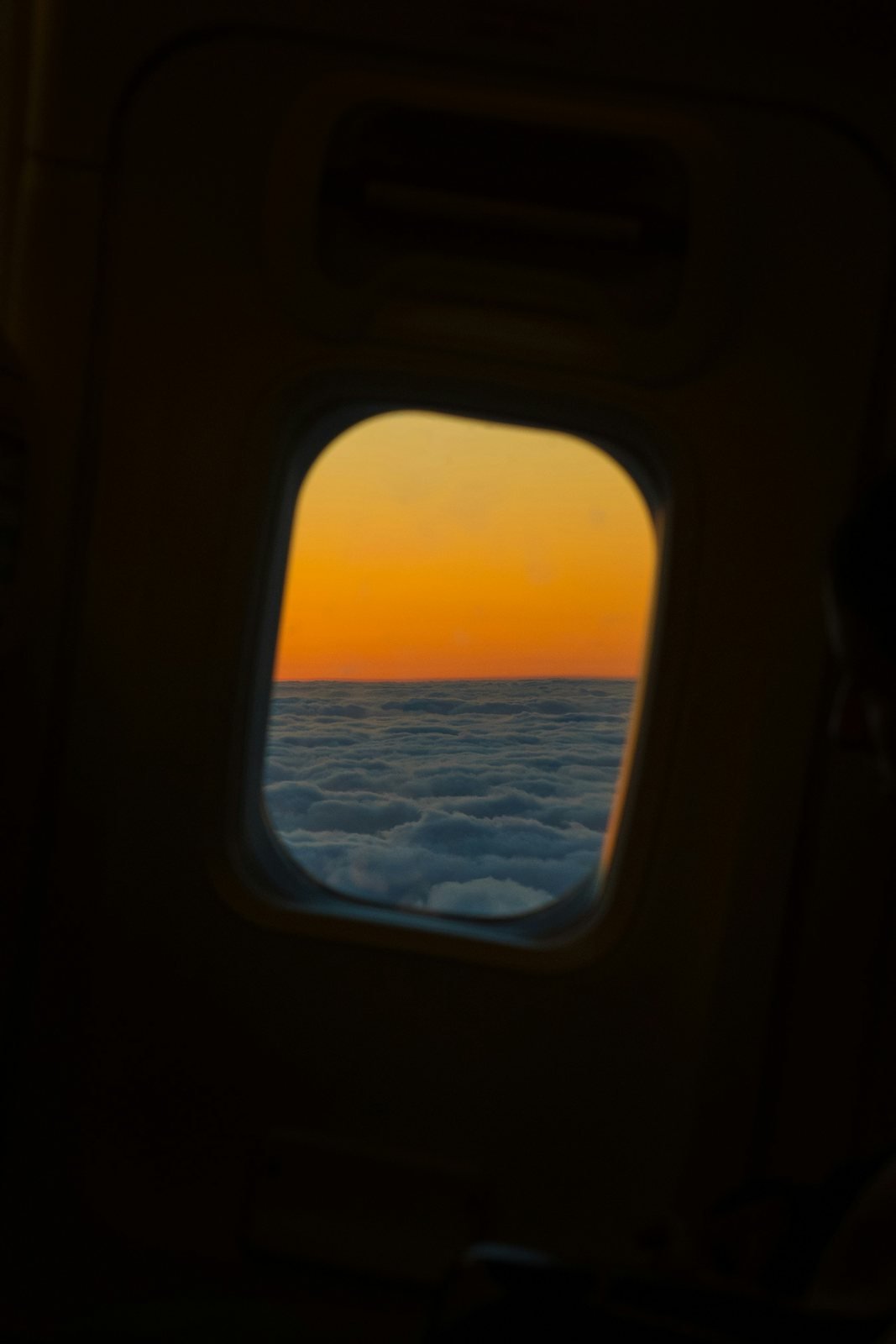 Orange sunset above clouds through an airplane window